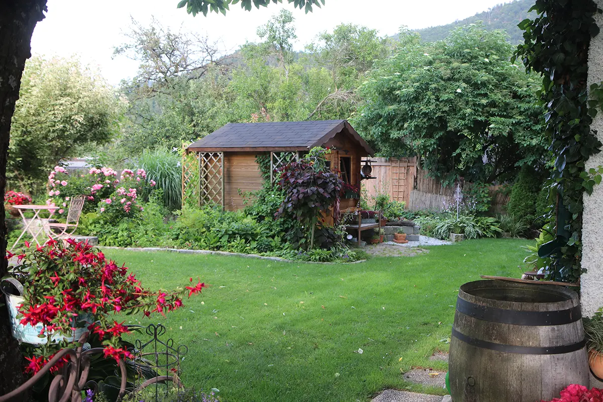 Blick auf eine Gartenhäuschen aus Holz, mitten in einem romantischen Garten, angelegt im typischen Cottage Garten Stil
