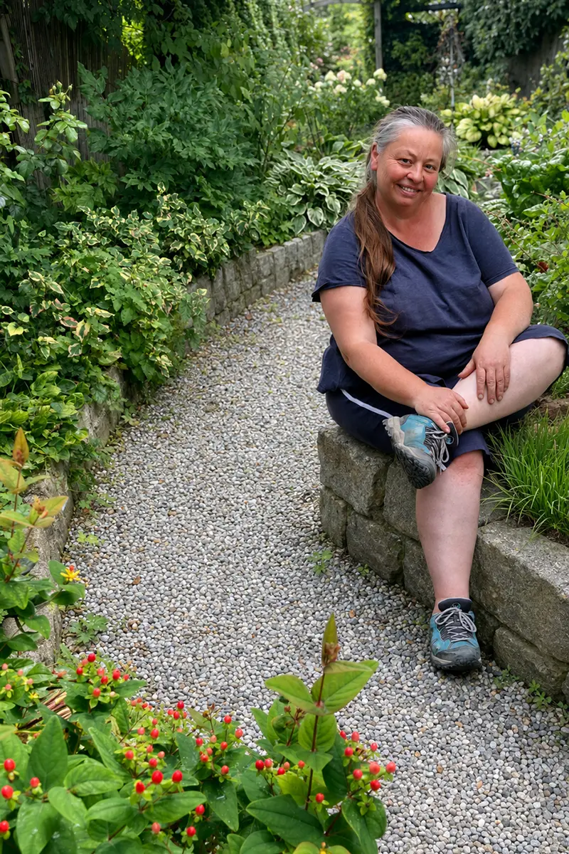 Gartengestalterin Isabella Pfenning sitzt auf einer kleinen Steinmauer in einem Garten den sie gestaltet hat.
